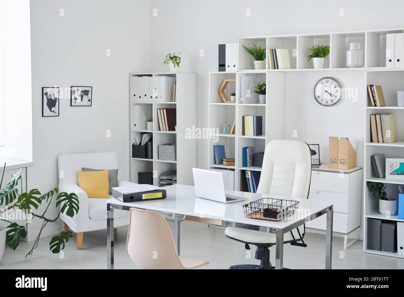Büro von Business Person mit Schreibtisch, Sessel von professionellen, Stuhl für Kunden, Regale, Uhr, grüne Pflanze und zwei Bilder an der Wand Stockfoto