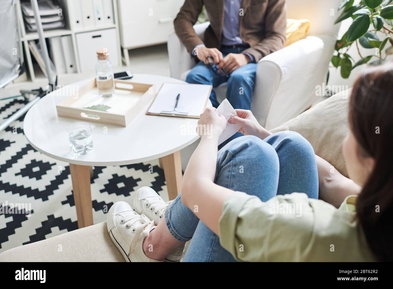 Junge verärgerte Frau mit Papiertuch in den Händen auf der Couch sitzend, weinend und Senior erfahrene Beraterin über ihre Probleme zu erzählen Stockfoto