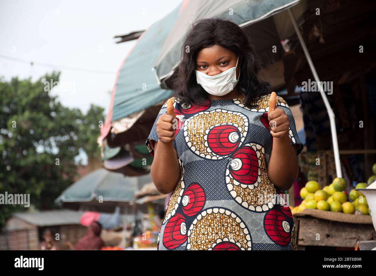 afrikanische Frau, die in einem Markt mit einer Gesichtsmaske mit Daumen nach oben tradet Stockfoto