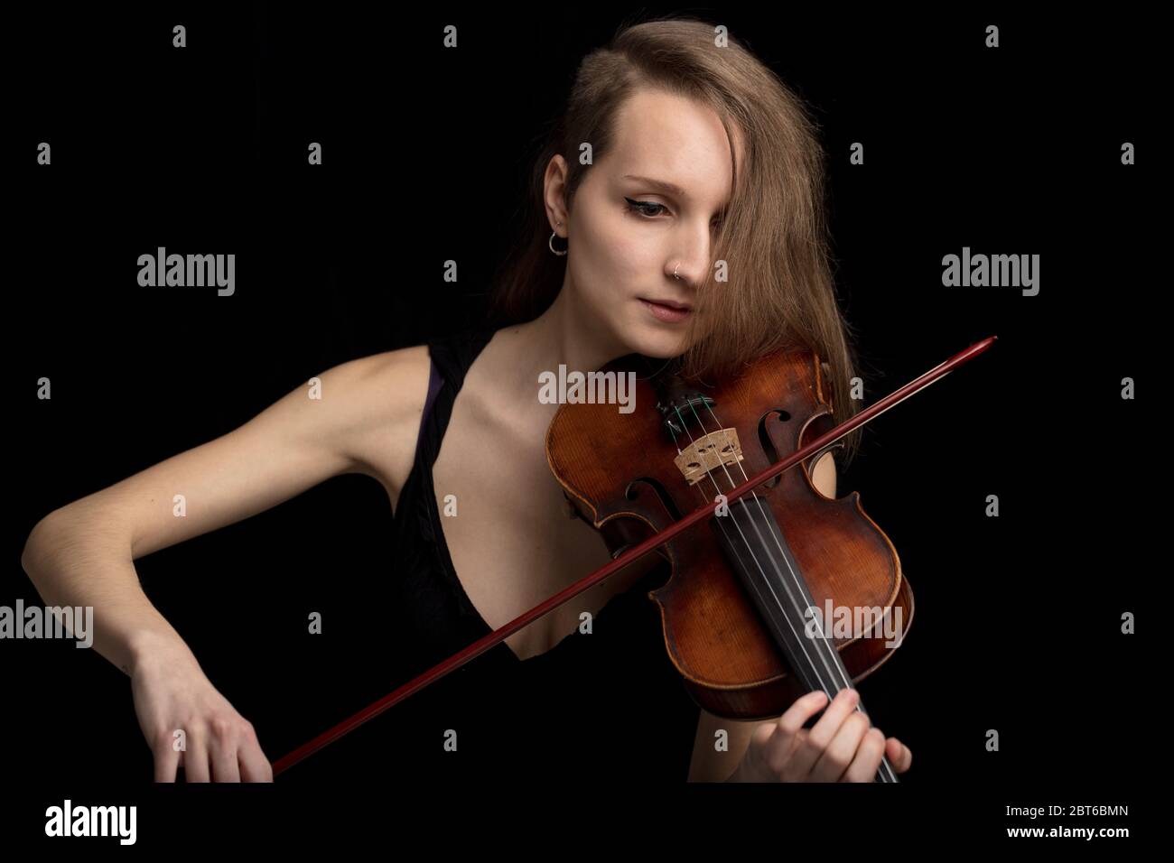 Trendy moderne Geigerin spielt auf einer handgefertigten antiken Barockgeige in einem klassischen Konzert oder Recital auf einem schwarzen Hintergrund Stockfoto