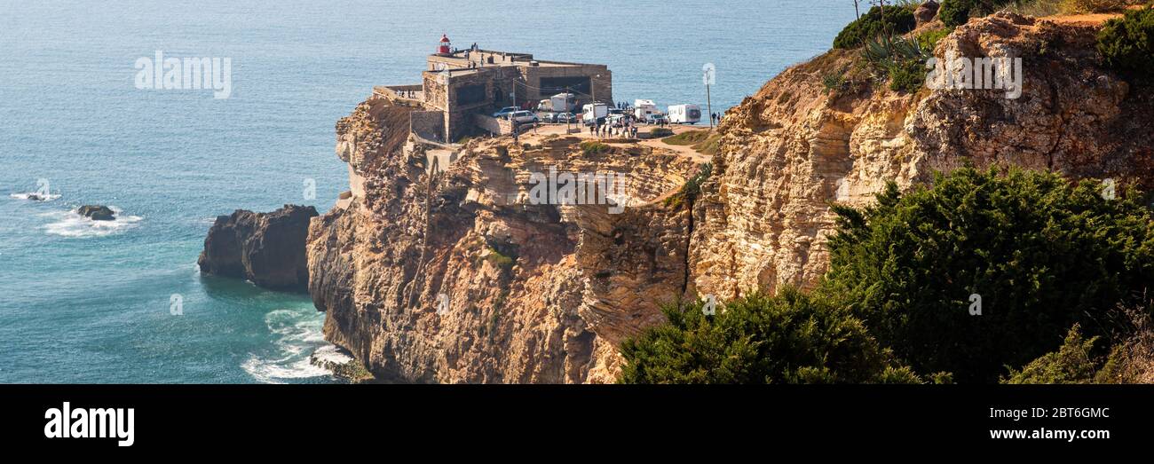 Alte Festung an der Küste von Portugal, Nazare. Leuchtturm auf der Felsklippe. Küste des Atlantiks. Die Hänge des Vorgebirges sind mit gree bedeckt Stockfoto