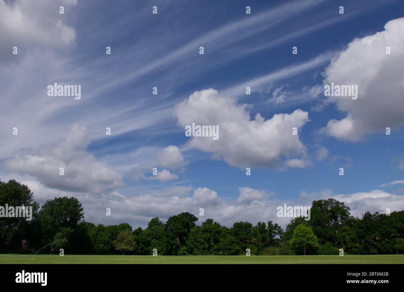 Ungewöhnliche Wolkenbildung am blauen Himmel über Bäumen und Grünflächen Stockfoto