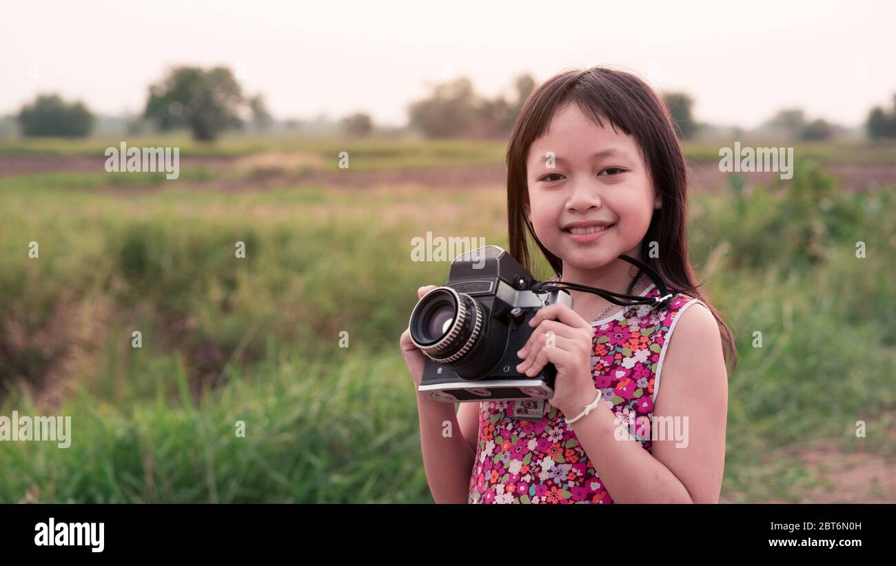 Kleines Mädchen mit Mittelformat-Filmkamera und das Fotografnen von Sonnenuntergang Landschaft mit grünen Feld Hintergrund Stockfoto