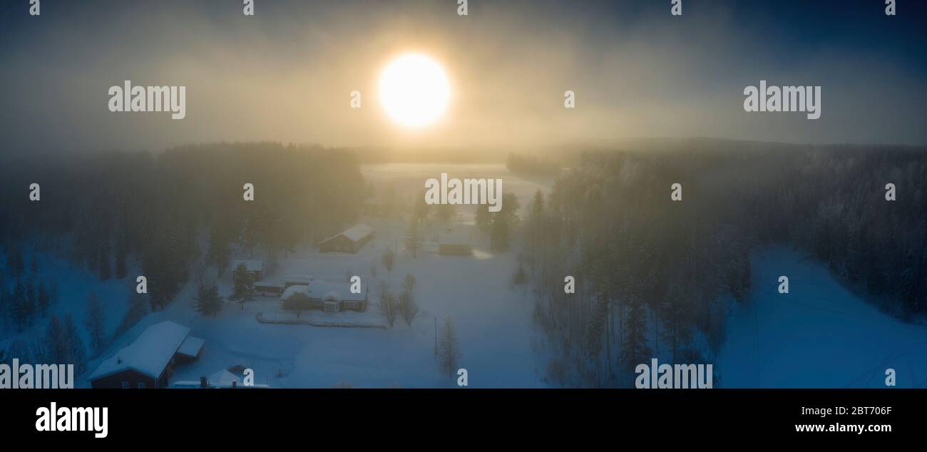 Majestätische Ansicht des Winteruntergangs mit sehr großem Sonnenfleck in gefrorener nebliger Luft, Winterkiefernwald, Luft, Grano Dorf, um Umea Stadt, Schweden Stockfoto