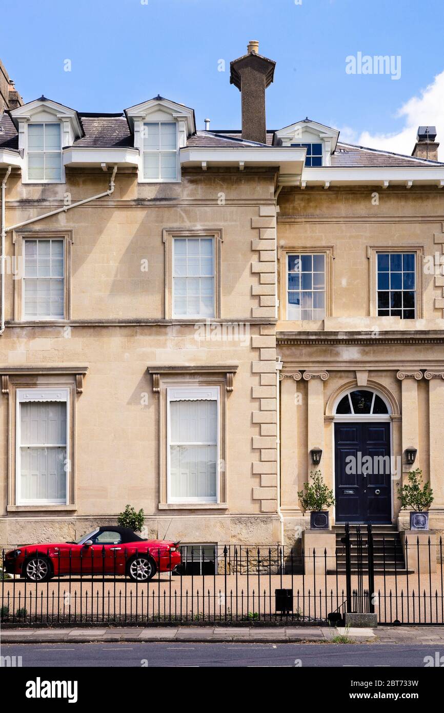 Wunderschönes Cotswold Steinstadthaus mit ikonischem roten Sportwagen, der draußen geparkt ist Stockfoto