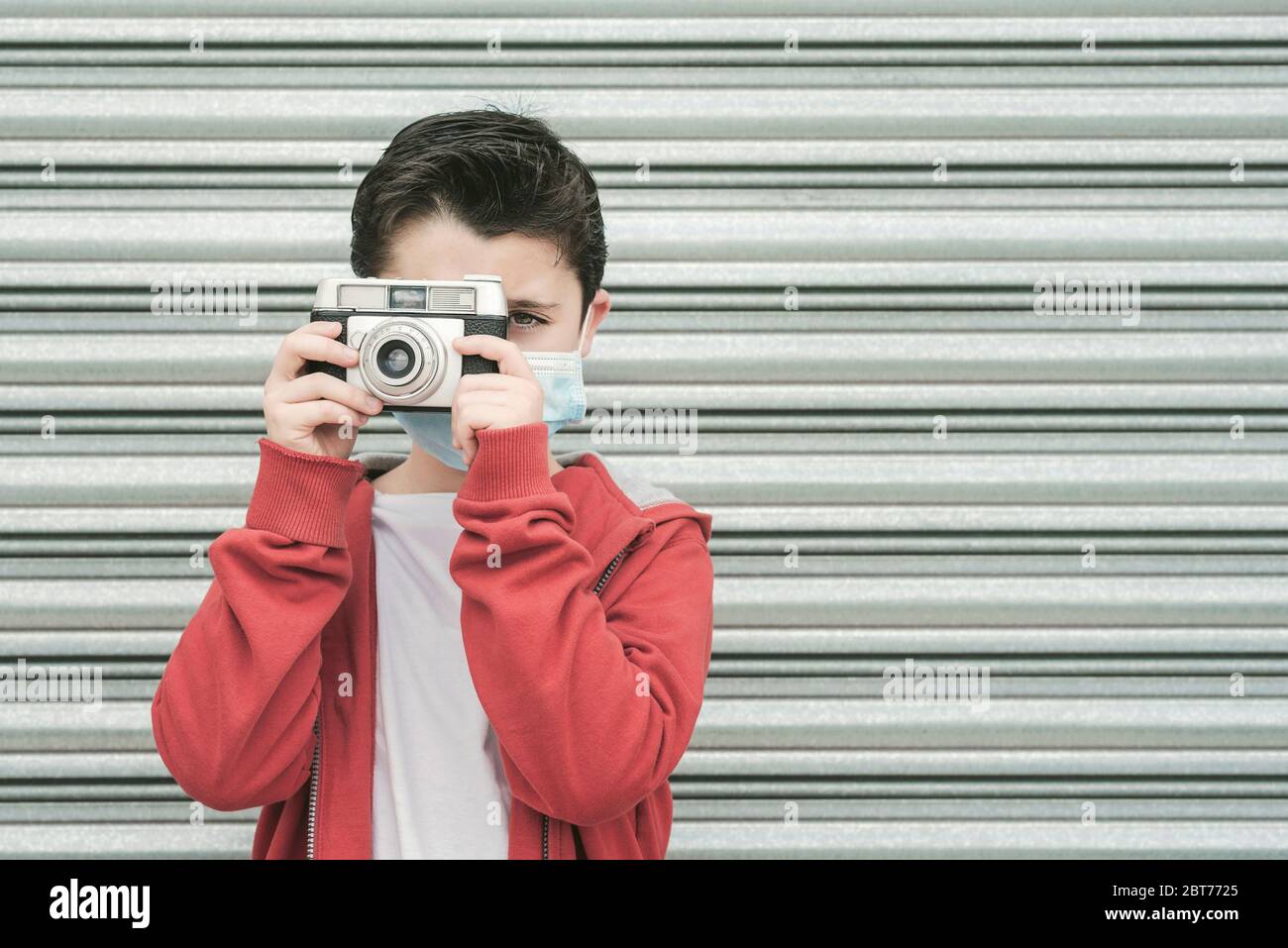 Kind mit medizinischen Maske nehmen Sie Fotos mit seiner Kamera im Freien Stockfoto
