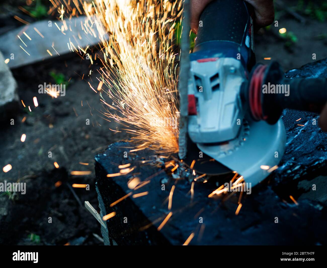 Arbeiter schneidet überschüssige Verstärkung im Fundament mit einem Winkelschleifer, Metall Funken fliegen Stockfoto