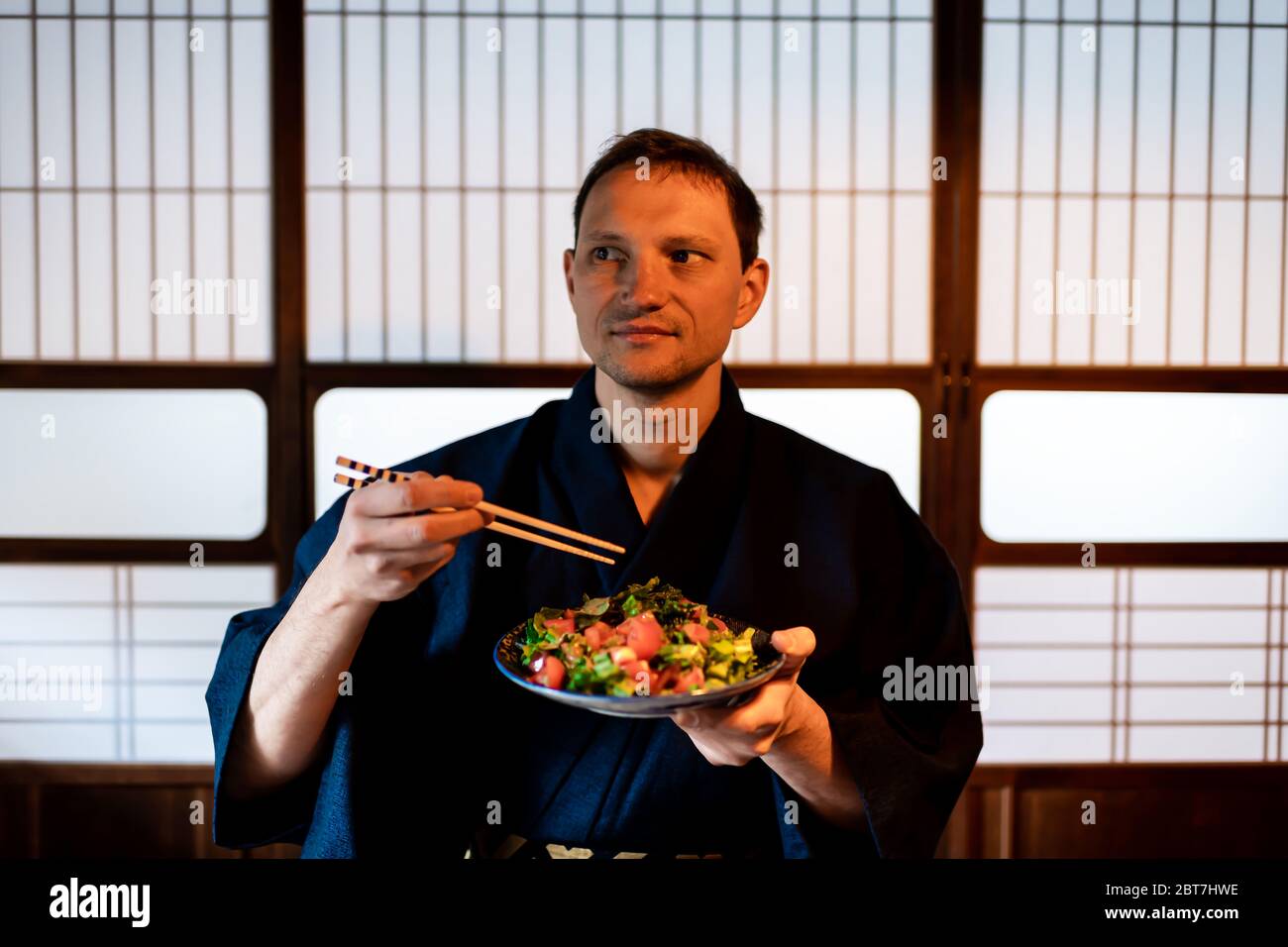 Traditionelles japanisches Haus oder Ryokan Restaurant mit einem Touristen in Kimono oder Yukata, der von einem Salatteller und im Hintergrund von Shoji-Türen isst Stockfoto