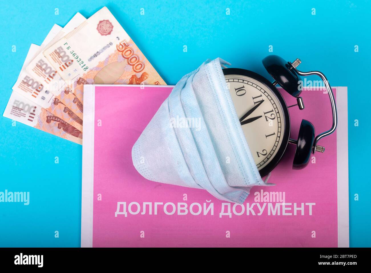 Schützende medizinische Maske auf schwarzem Wecker liegt auf Schuldenmeldedokument mit der Inschrift in russischem 'Zahlungsdokument' und russischem Geld auf einer cy Stockfoto