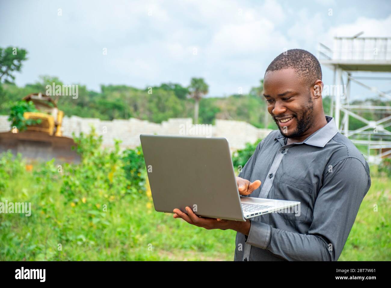 Junger afrikanischer Geschäftsmann, der einen Laptop auf einem Grundstück benutzt Stockfoto