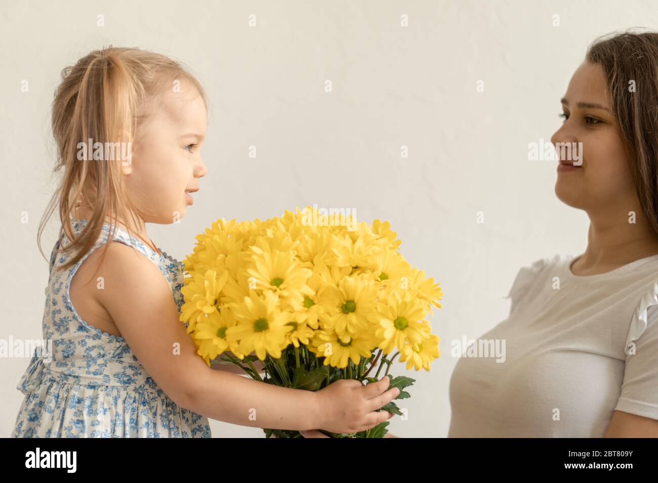 Mutterschaft, Muttertag, Geburtstag, Kindheit, Familienkonzept - close-up kleines Mädchen in blau bunten Kleid gratulieren und geben junge Mutter hell Stockfoto