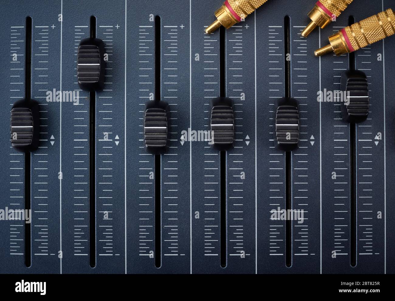 Audiokabel mit goldenen rca-Anschlüssen an Fadern eines Mischers für die Audioproduktion Stockfoto
