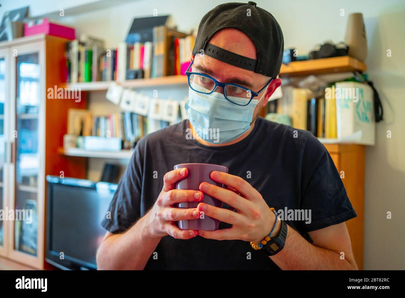 Mann trinkt Kaffee in medizinischen Maske Morgen zu Hause auf Corona-Virus Selbstisolierung. Pandemie Quarantäne. Virenschutzmaske. Masken zum Schutz vor Viren. Stockfoto