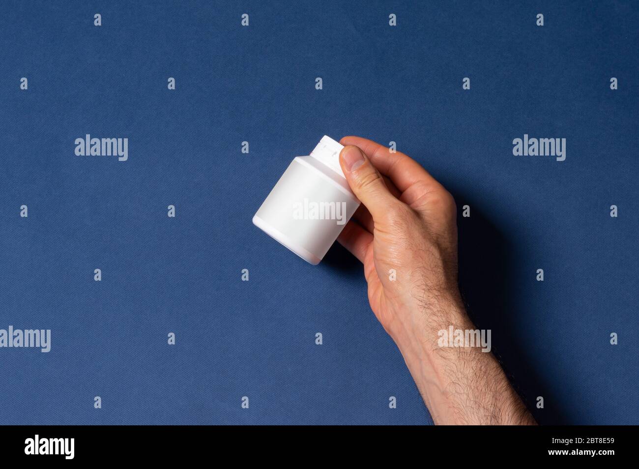 Männliche Hand hält eine weiße Pillbox Flasche vor blauem Hintergrund, Mock-up-Serie Vorlage bereit für Ihr Design, Abdeckung Auswahlweg enthalten Stockfoto