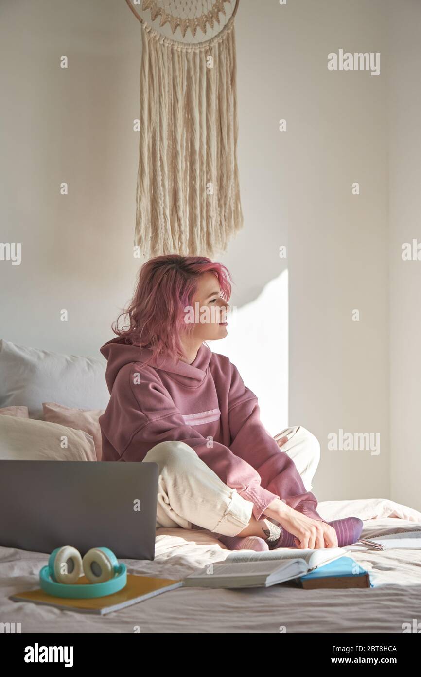 Teen Mädchen mit rosa Haar trägt Hoodie sitzen im Bett denken wegschauen. Stockfoto