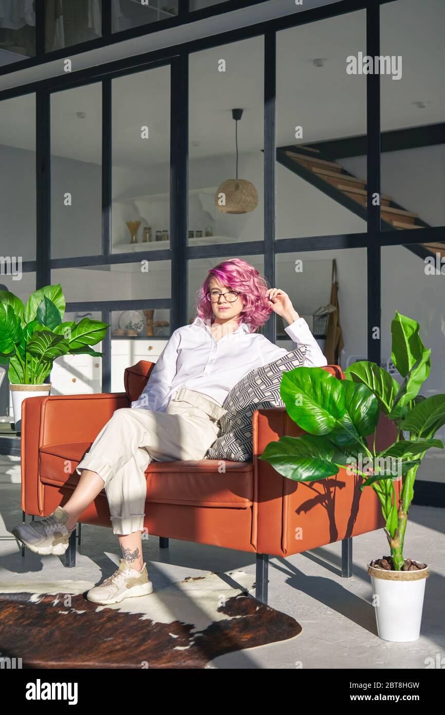 Entspannte Hipster-Frau mit rosa Haar Lounge auf Sofa in modernen gemütlichen Wohnzimmer. Stockfoto