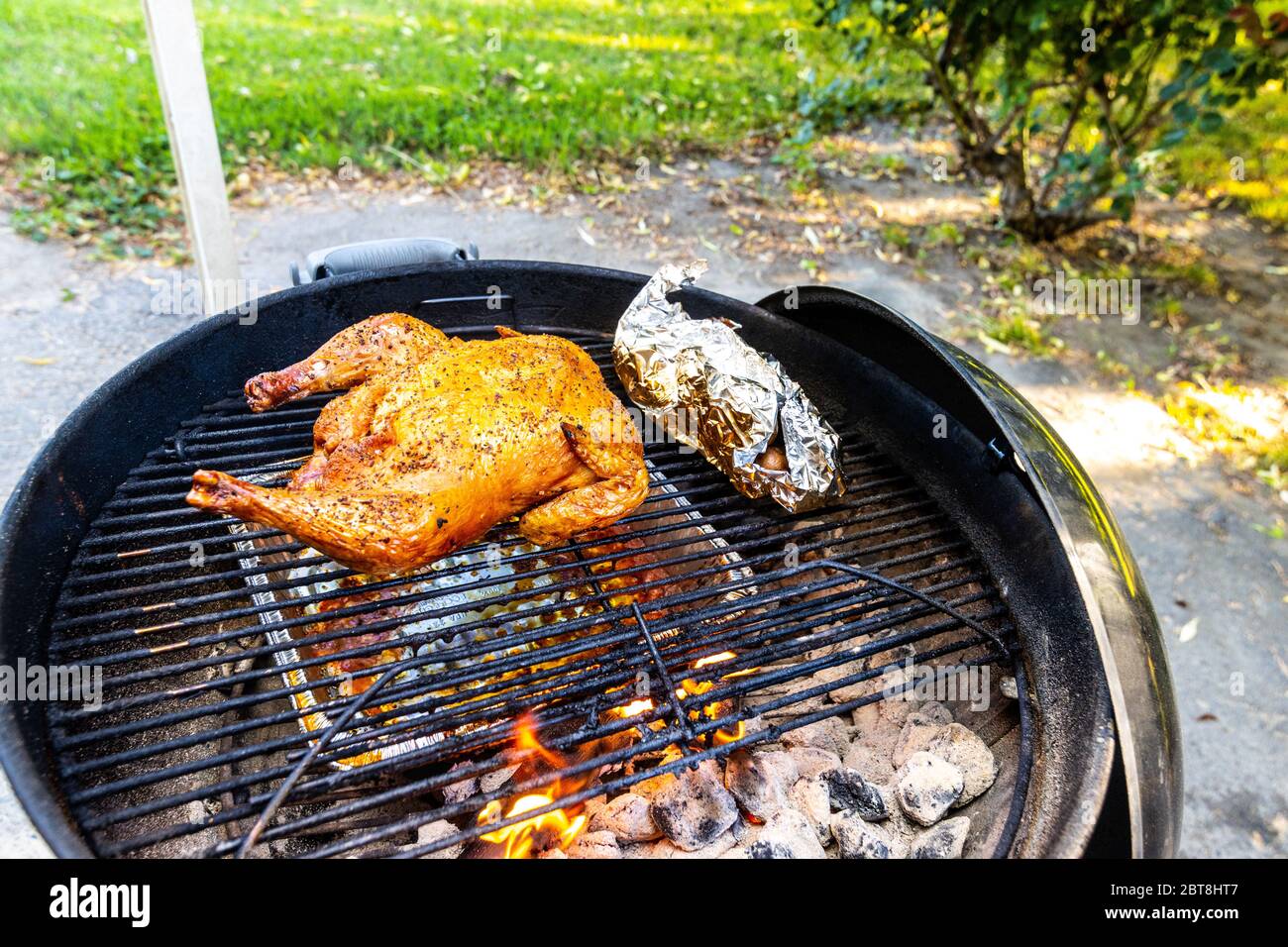 Ein ganzes Huhn, das mit Apfelholz auf einem Weber Kessel Grill mit einem  Päckchen Kartoffeln und Karotten geräuchert wird Stockfotografie - Alamy