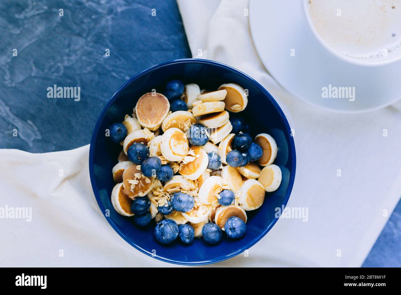 Nahaufnahme von Mini Pancake Müsli, Mini Pfannkuchen in einer dunkelblauen Schüssel mit Ahornsirup Honig mit Heidelbeere. Hintergrund der Speisen. Stockfoto