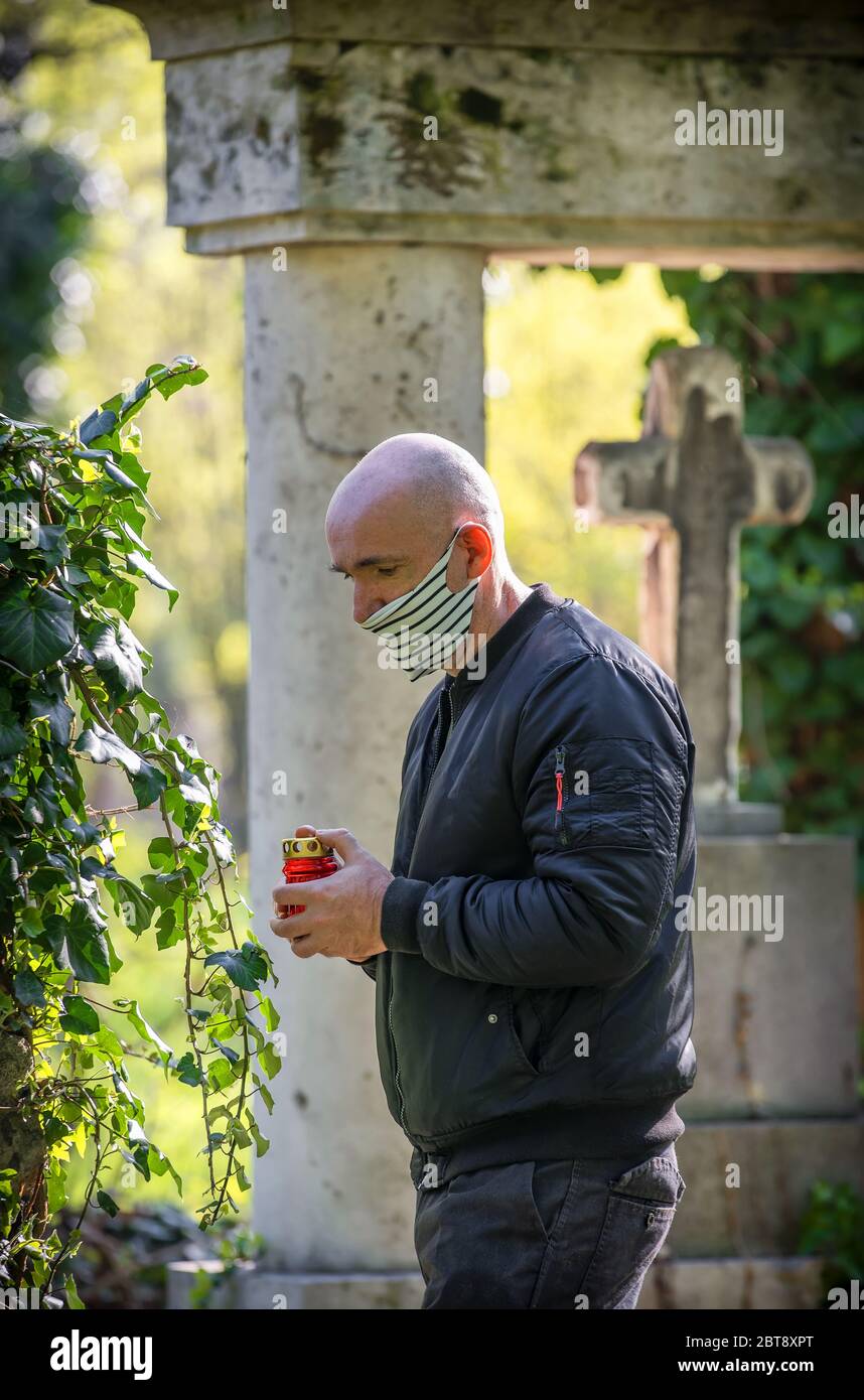 Auf dem Friedhof erinnert ein Mann an seinen verlorenen Verwandten, der eine Gesichtsmaske trägt, die durch den Virus Covid - 19 verursacht wurde. Stockfoto