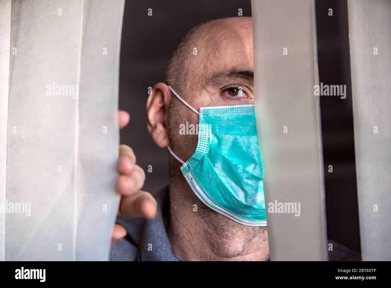 Der Mann, der medizinische Maske trägt, schaut durch das Fenster. Isolation zu Hause für Virenausbruch. Konzept Haus selbst Quarantäne, Prävention COVID-19. Stockfoto