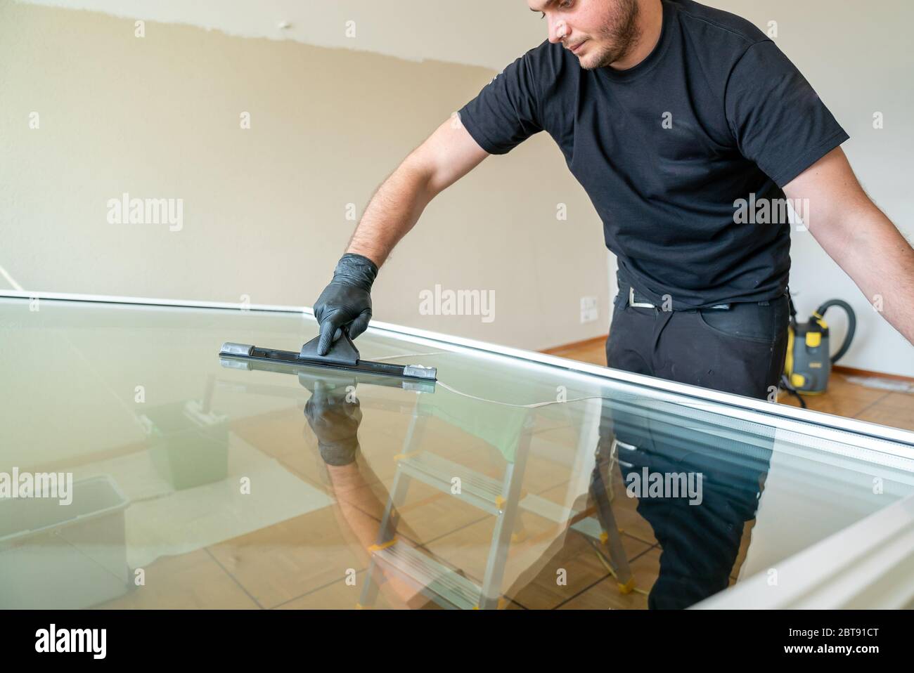 Ein professioneller Reiniger, der ein großes Fenster mit einem Abzieher und einem Schaber reinigt Stockfoto