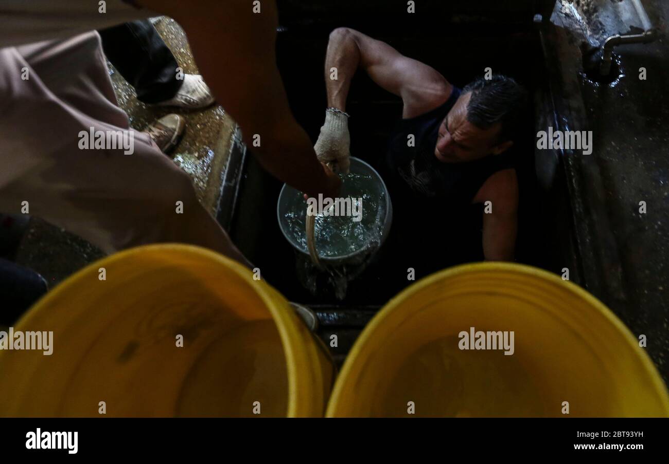 Caracas, Venezuela. Mai 2020. Männer sammeln Trinkwasser aus einem unterirdischen Brunnen im Bezirk Catia in Eimern. Viele Haushalte im Land haben kein fließendes Wasser mehr. Die Wasserversorgung funktioniert teilweise nicht mehr. Die Coronavirus-Pandemie verschlimmert die Situation noch. Quelle: Pedro Rances Mattey/dpa/Alamy Live News Stockfoto