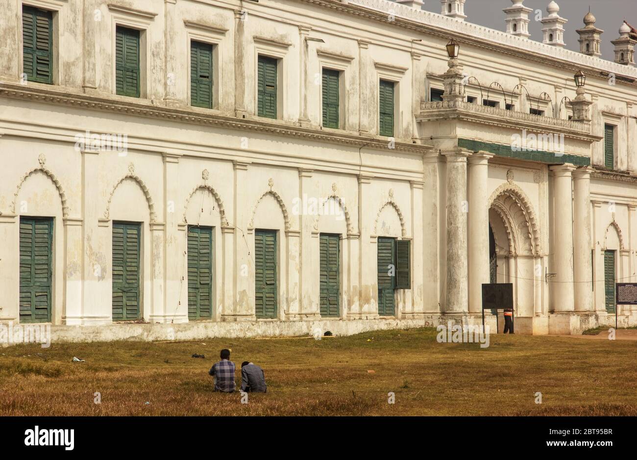 Murshidabad, Westbengalen/Indien - Januar 15 2018: Zwei Personen sitzen auf den Gärten vor der imposanten Außenfassade des Nizamat Imambara. Stockfoto