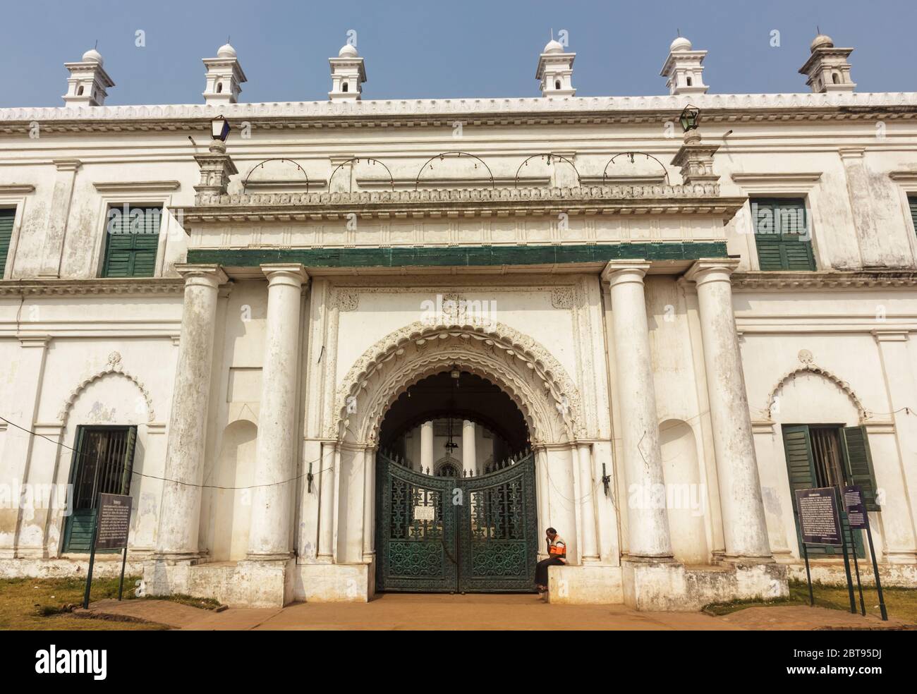 Murshidabad, Westbengalen/Indien - Januar 15 2018: Ein Hausmeister sitzt auf einem Regal außerhalb der Außenfassade und Tür von Nizamat Imambara. Stockfoto