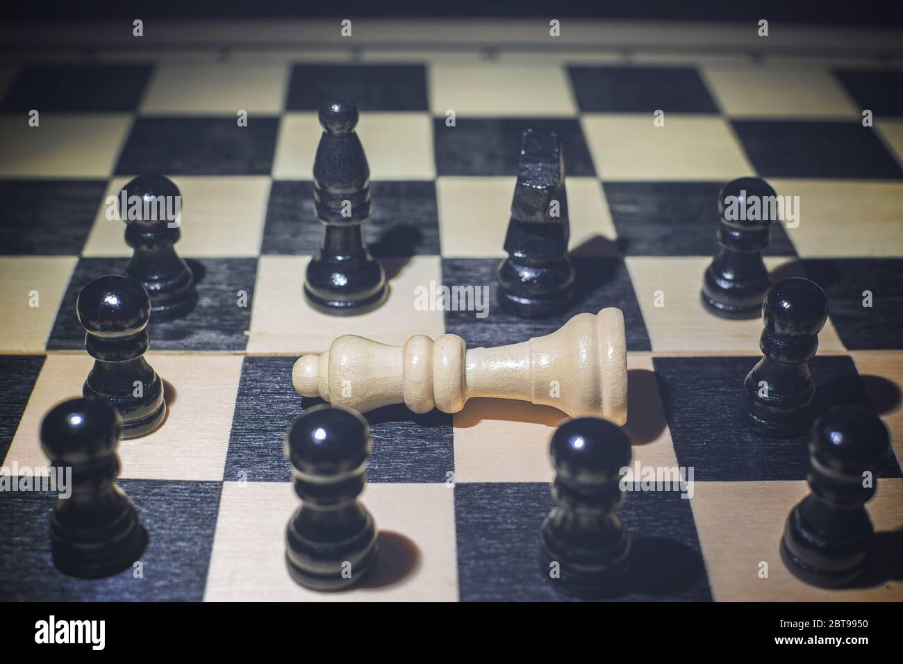 Weiße Königin fiel auf das Schachbrett und um die schwarzen Stücke Stockfoto
