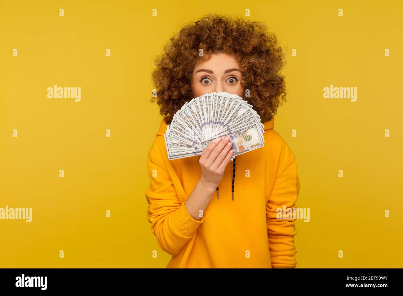 Porträt der überrascht lockig-haarige Frau im urbanen Stil Hoodie spähe aus Geld mit staunen Augen, Freude Glück im Lotto, zeigt Haufen Puppe Stockfoto