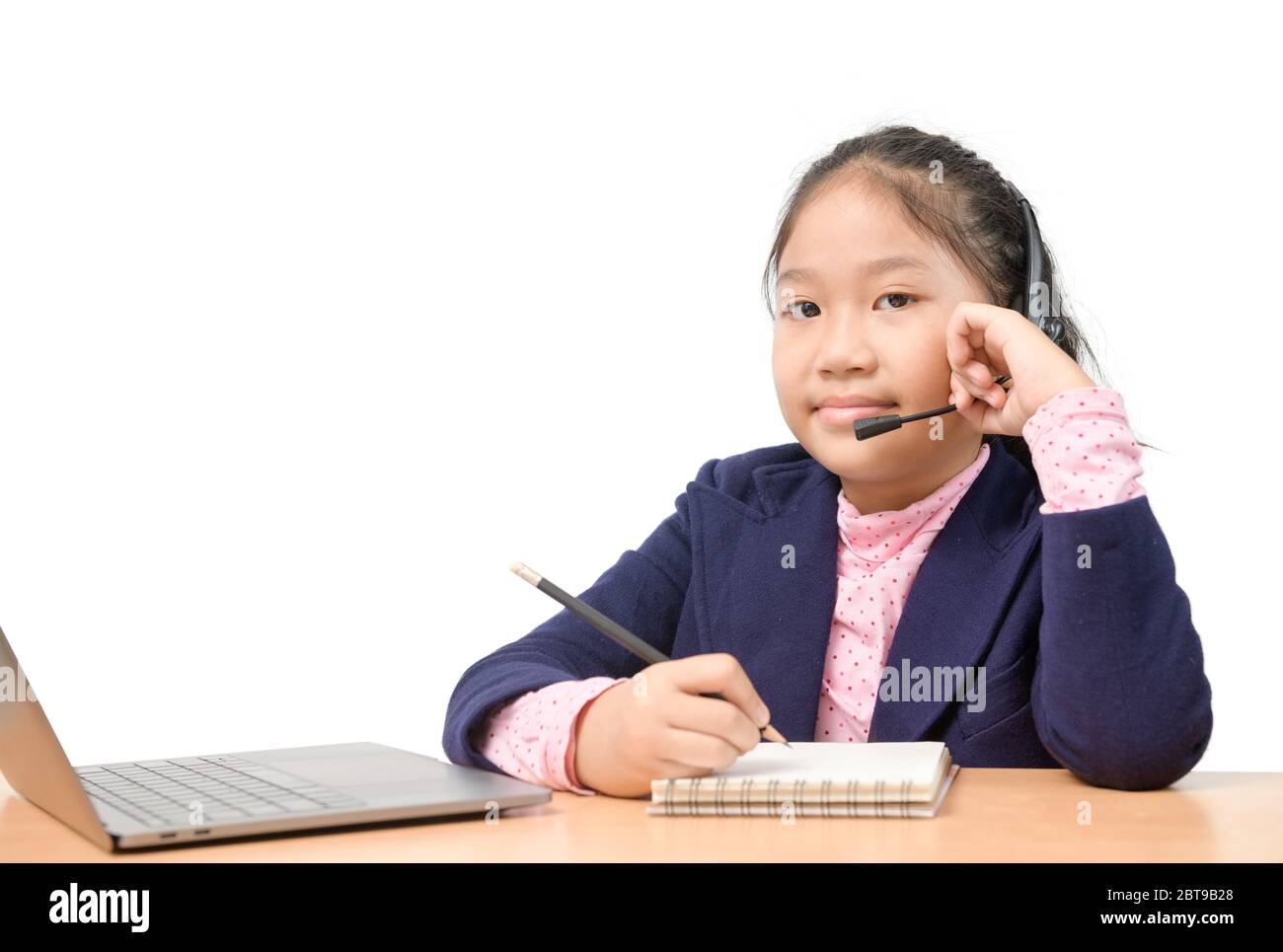 Nette asiatische Schulmädchen trägt ein Headset und Hausaufgaben zu tun, beobachten Lehrer online unterrichten über Laptop aufgrund des Ausbruchs der Koronarvirus oder Cov Stockfoto