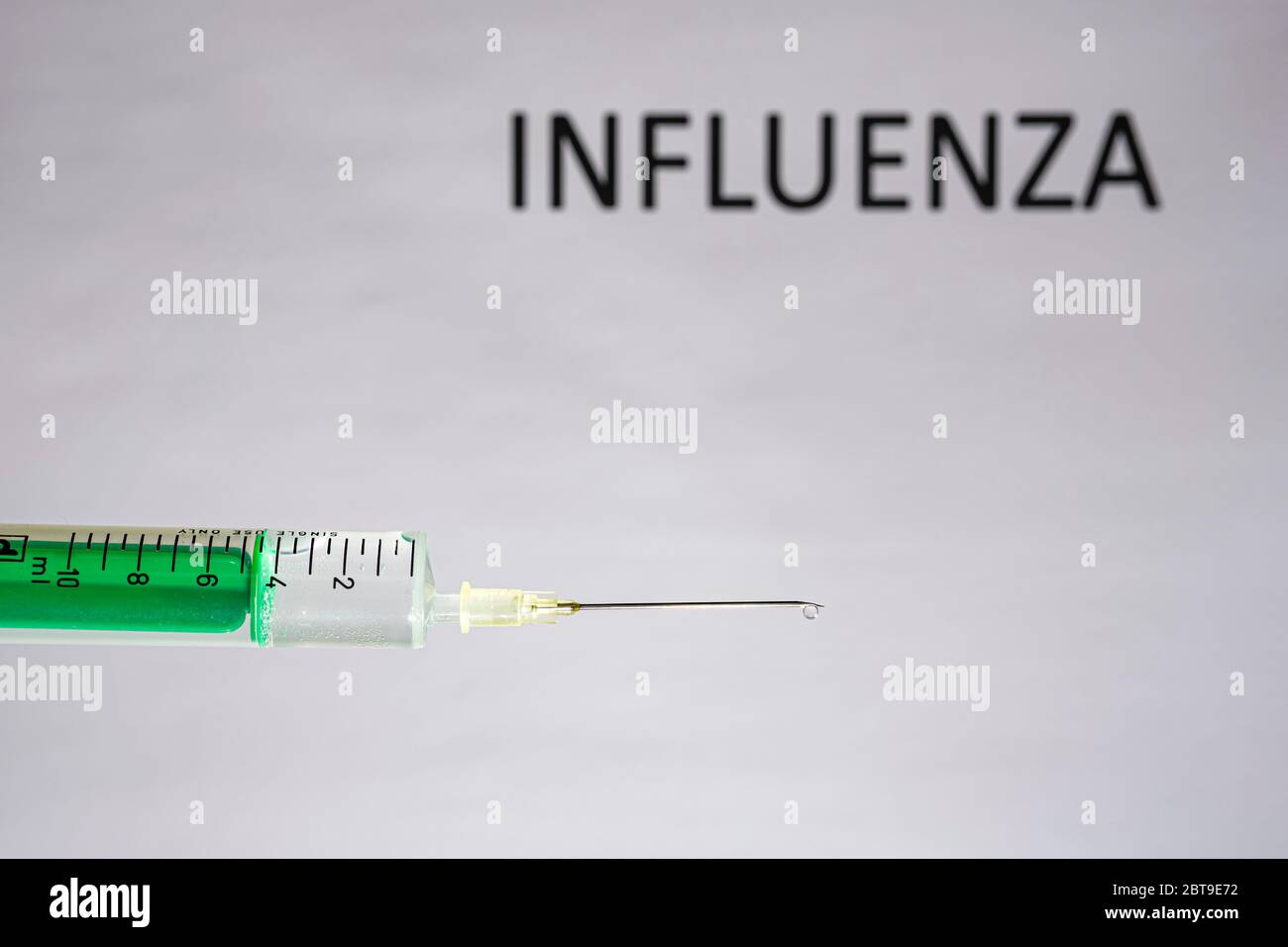 Diese Abbildung zeigt eine Einweg-Spritze mit einer hypodermischen Nadel, INFLUENZA, die auf einer weißen Tafel dahinter steht Stockfoto