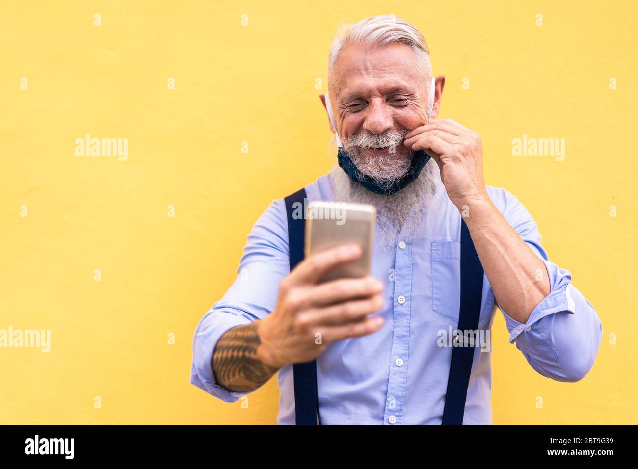 Trendy Hipster Mann mit Handy tun Videoanruf während der Mode Seide Sicherheitsmaske tragen - Outfit, Technologie und Lifestyle während Coronavirus ti Stockfoto