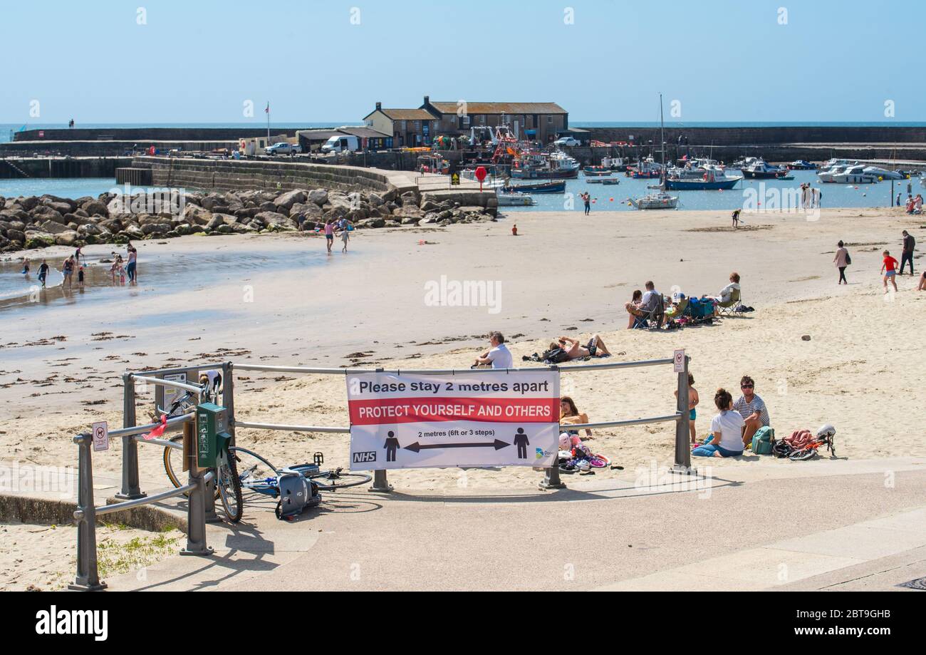 Lyme Regis, Dorset, Großbritannien. Mai 2020. UK Wetter: Einheimische und Familien strömen an den Strand, um die glühenden heißen Sonnenschein im Badeort Lyme Regis genießen. Ein Schild in der Nähe des Cobb erinnert Strandbesucher daran, soziale Distanz zu verfolgen und 2 Meter voneinander entfernt zu bleiben. Kredit: Celia McMahon/Alamy Live News Stockfoto