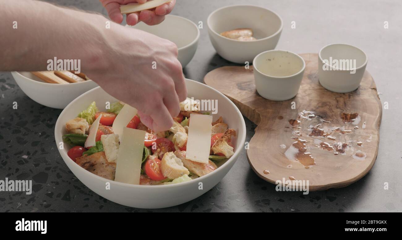 Man Hand geben Sie Parmesan Käse auf caesar Salat in weiß Keramikschale auf Betonplatte Stockfoto