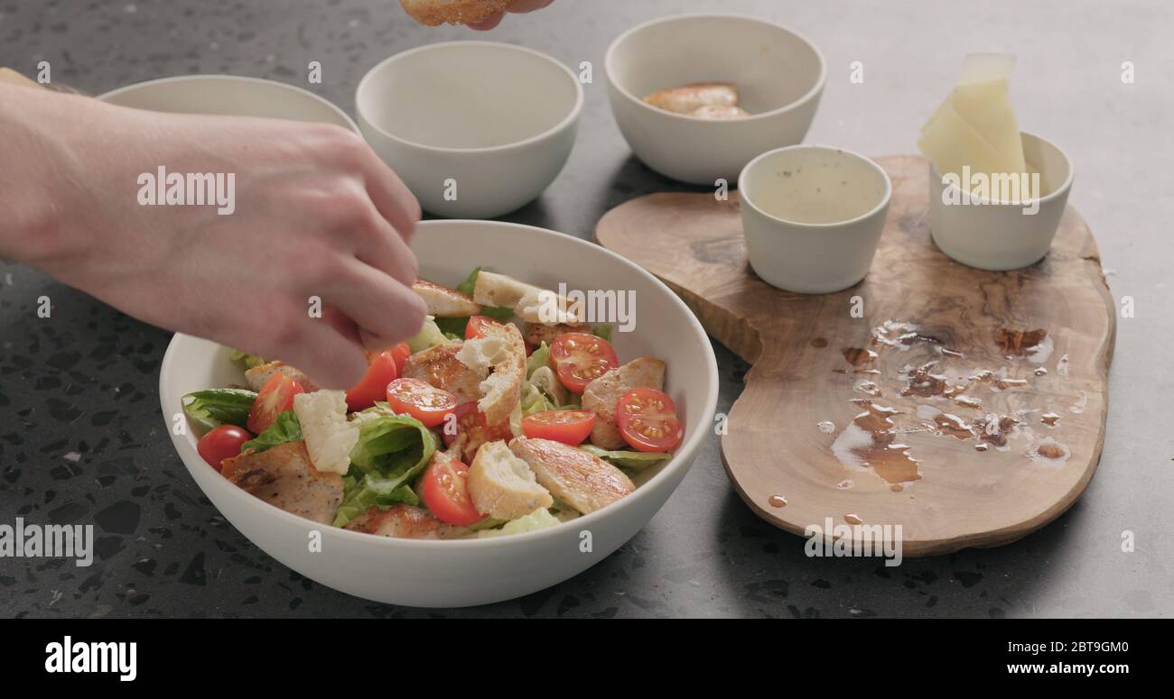Man Hand fügen Croutons auf caesar Salat in weißer Keramik Schüssel auf Betonplatte Stockfoto