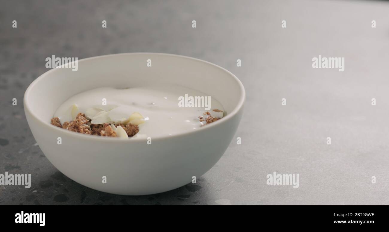 Joghurt über Schokoladengranola in weißer Schale auf Terrazzo-Oberfläche Stockfoto