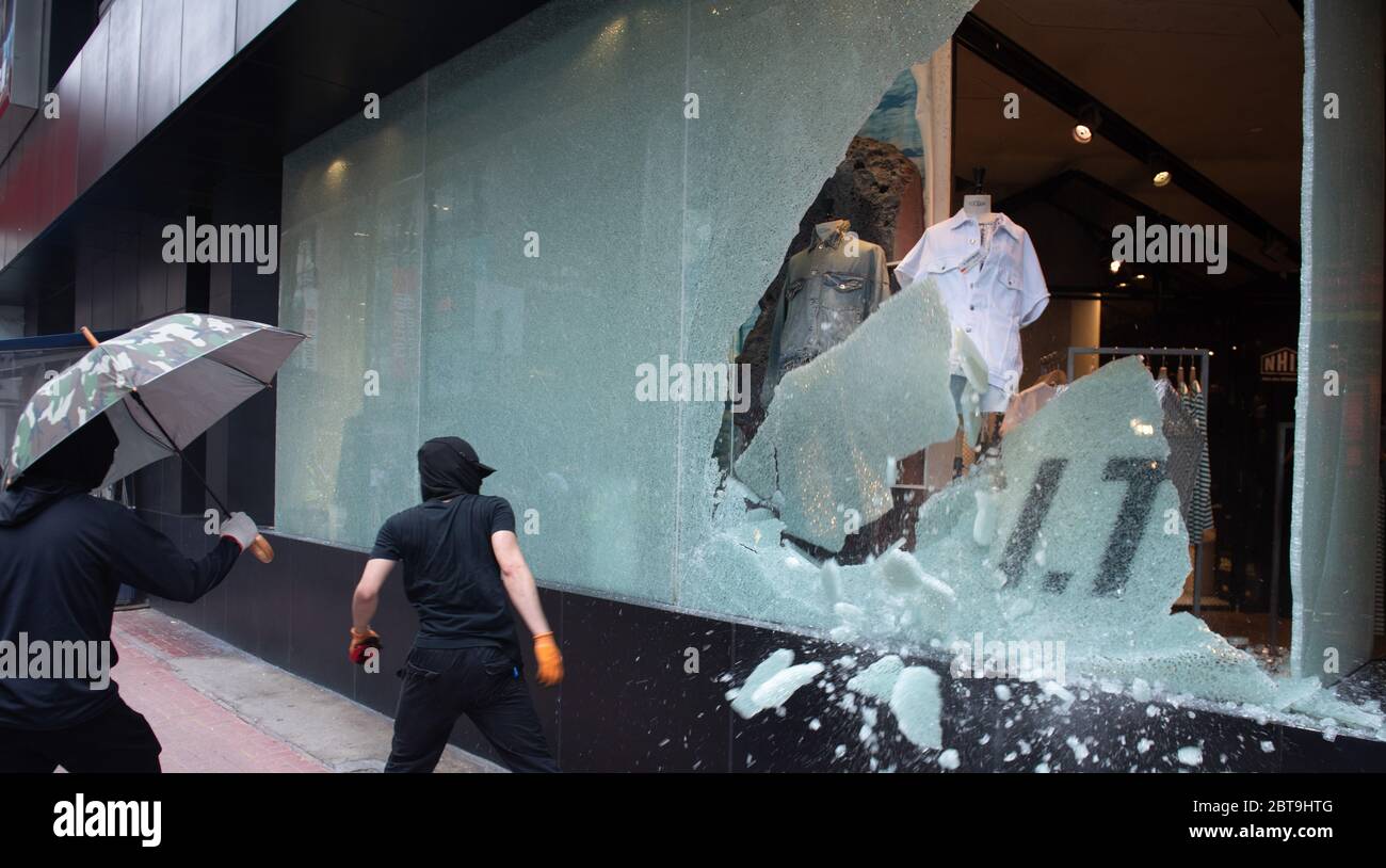 Ein Protestierender zerschlägt während der Demonstration die Fenster eines Bekleidungseinzelhandels.Tausende Demonstranten versuchten, gegen das vom Nationalen Volkskongress ausgearbeitete nationale Sicherheitsgesetz zu marschieren. Die Polizei benutzte Tränengas und verschiedene Geschosse, um Menschenmengen zu zerstreuen, während die Demonstranten Straßenblockaden schufen, bevor sie sich zurückkehrten. Stockfoto