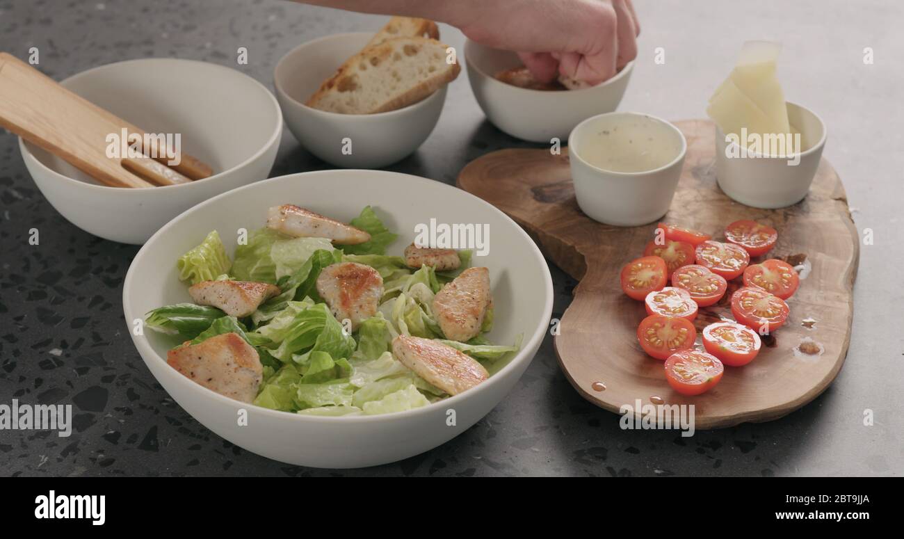 Man Hand fügen Sie Kirschtomaten und Huhn auf caesar Salat In weißer Keramikschale auf Betonplatte Stockfoto