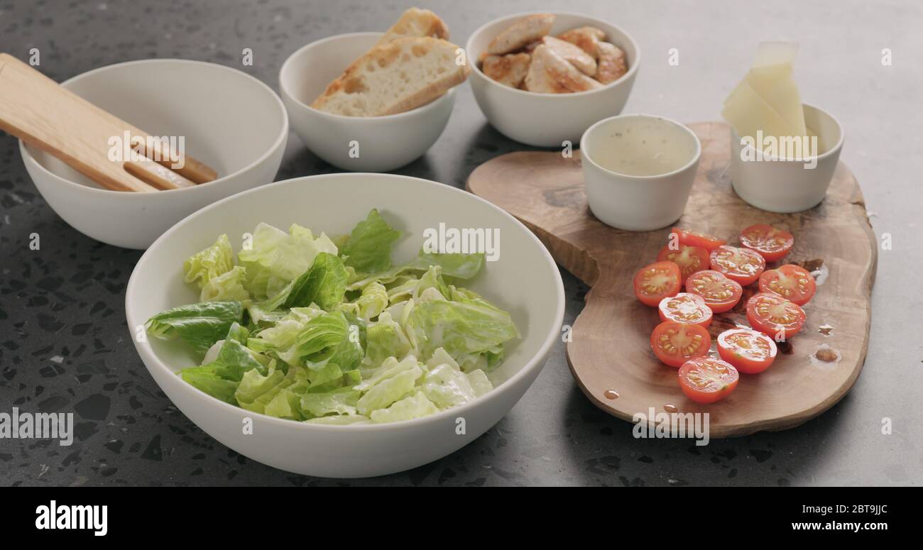 Man Hand mischen Romaine Salat und Dressing caesar zu machen Salat in weißer Keramikschale auf Betonplatte Stockfoto
