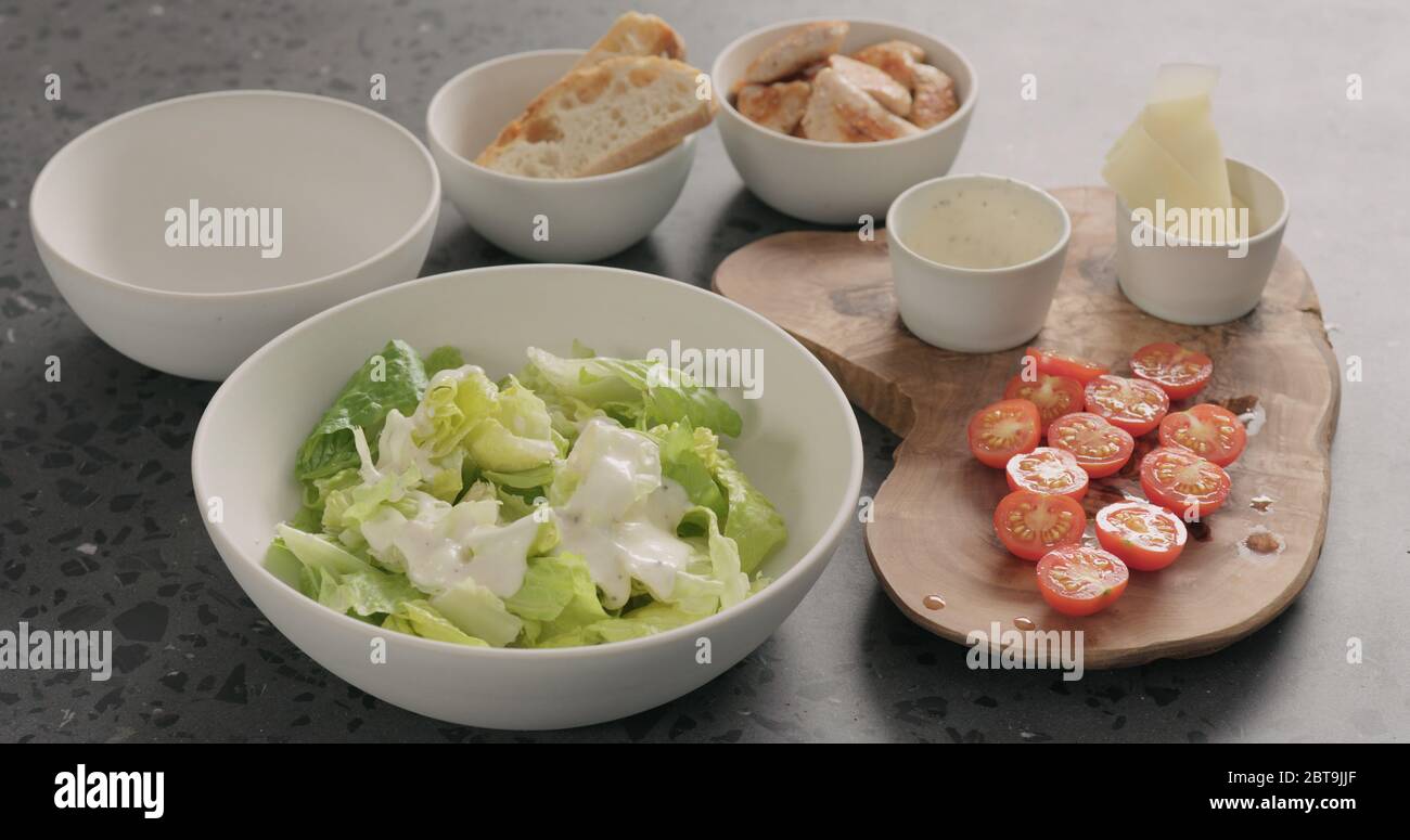 Man Hand mischen Romaine Salat und Dressing caesar zu machen Salat in weißer Keramikschale auf Betonplatte Stockfoto