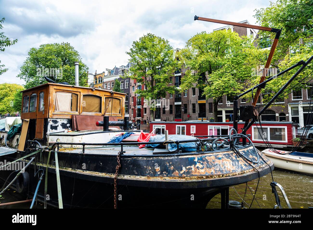 Altes rostig Schiff und ein Hausboot an einem Kanal in Amsterdam, Niederlande Stockfoto