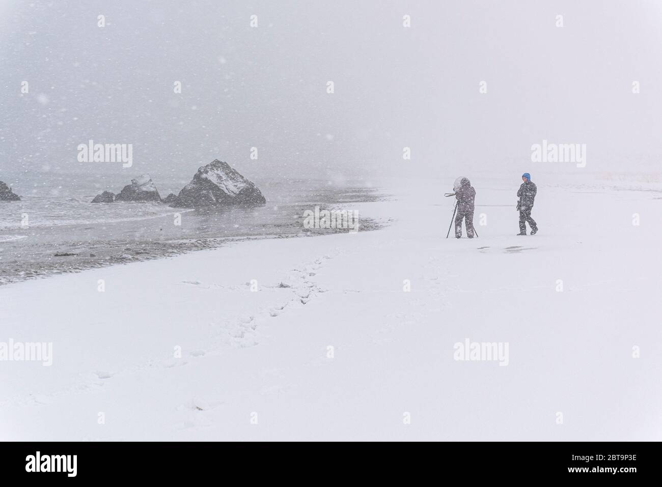 Unkenntlich erkennbare Person, die einen Felsen am Strand während eines windigen Schneesturms fotografiert Stockfoto