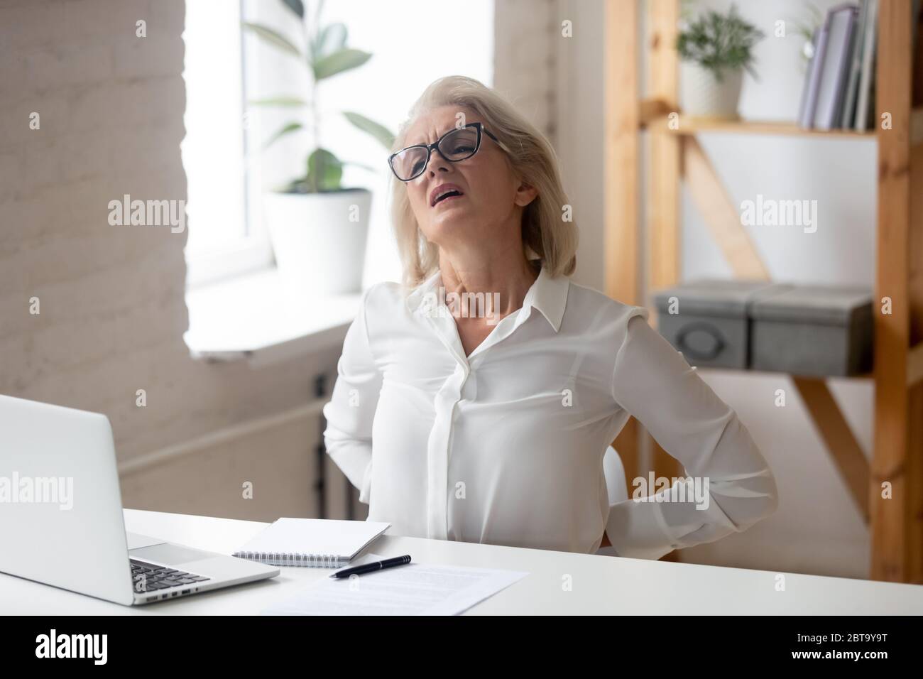 Weibliche Angestellte mittleren Alters leiden an Rückenschmerzen Stockfoto