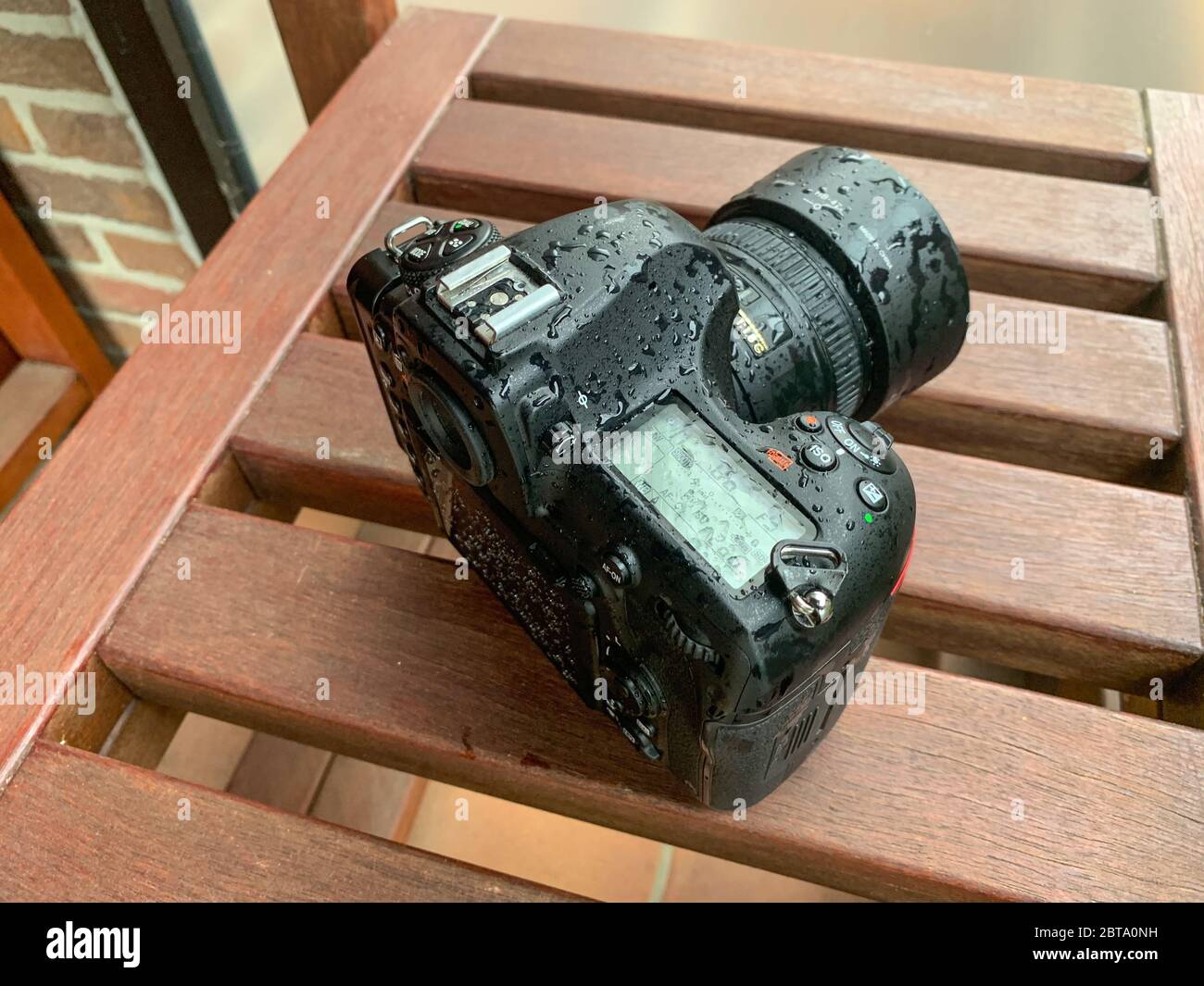Eine Spiegelreflexkamera (DSLR) ist vom Regen mit einem Objektiv mit Festbrennweite auf einem Holztisch nass Stockfoto