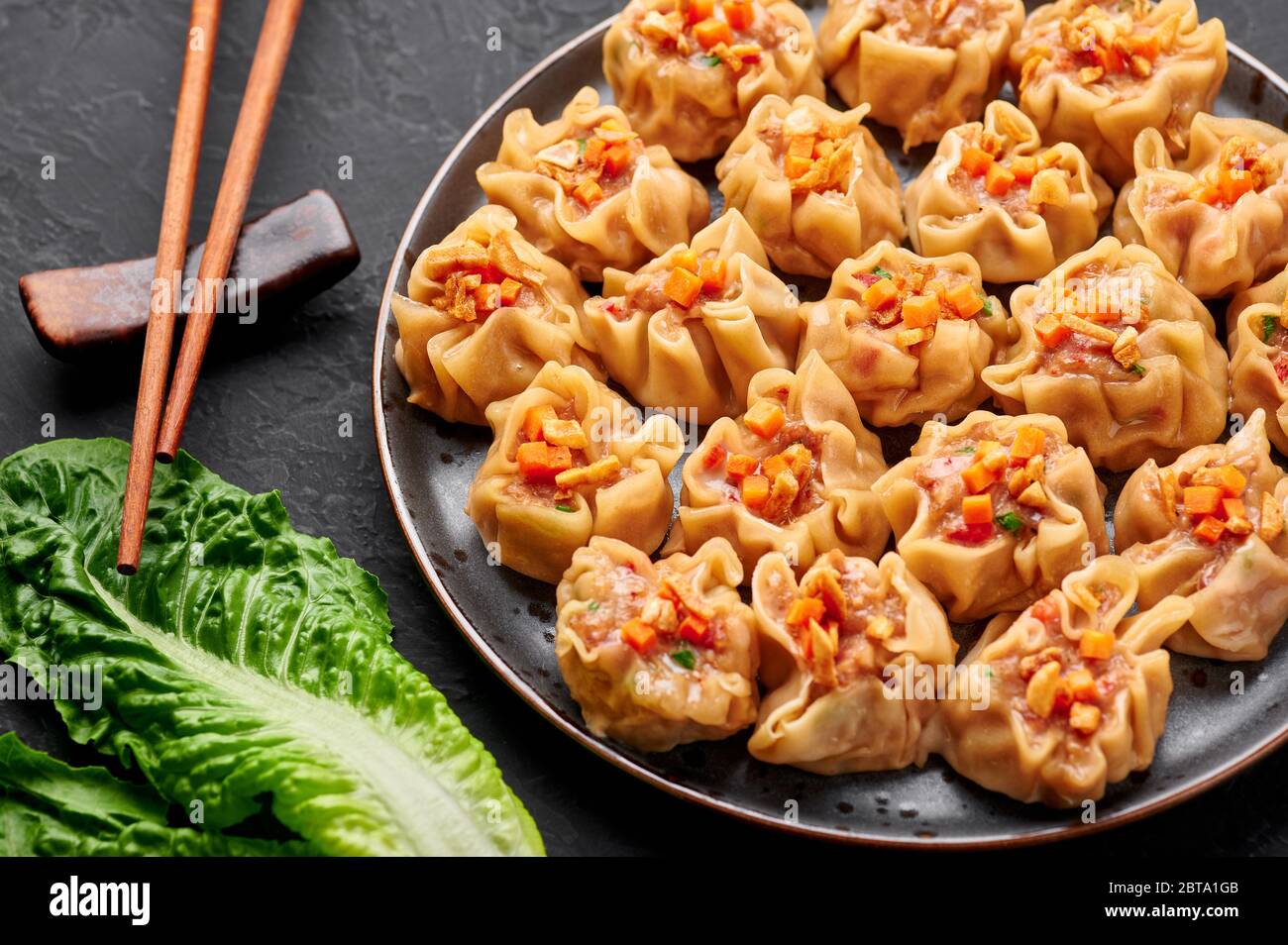 Shumai oder Kanom Jeeb oder gedämpfte Schweinefleisch- und Garnelenknödel auf einem schwarzen Teller auf dunklem Schieferhintergrund. Shumai ist ein chinesisches Gericht mit Hackfleisch m Stockfoto