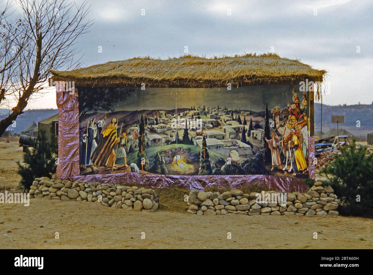 Ein Gebäude, in dem eine Krippe auf einer Basis für die 40. Infanterie der US-Armee, Division Replacement Company während des Koreakriegs, Südkorea, 1953, untergebracht ist. Das eindrucksvoll bemalte Wandbild von Bethlehem zeigt Hirten und die drei Weisen. Es ist beleuchtet und vor den Elementen mit einem Strohdach geschützt. Stockfoto