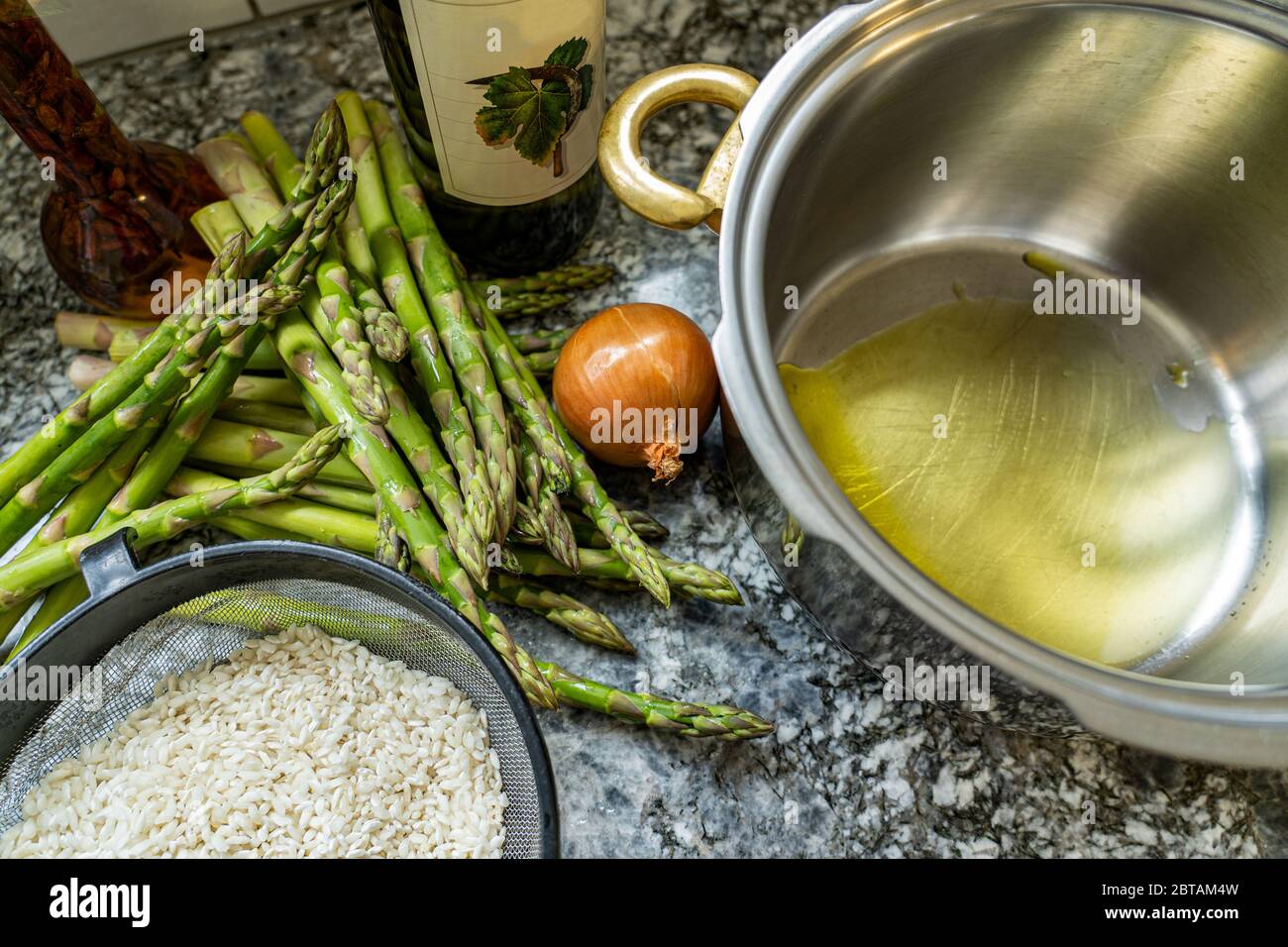Risotto Reis mit Spargel, Zwiebeln und Weißwein kochen. Pfanne mit Olivenöl auf Granit Hintergrund. Hohe Winkelansicht. Stockfoto