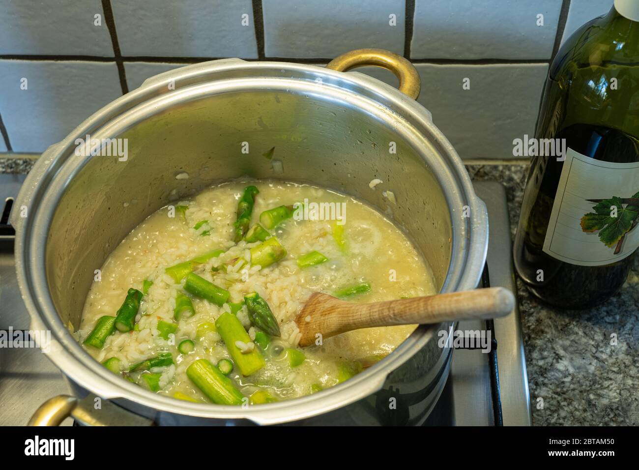 Risotto Reis mit Spargel, Zwiebeln und Weißwein kochen. Holzlöffel in der Pfanne mit Reis. Hohe Winkelansicht. Stockfoto