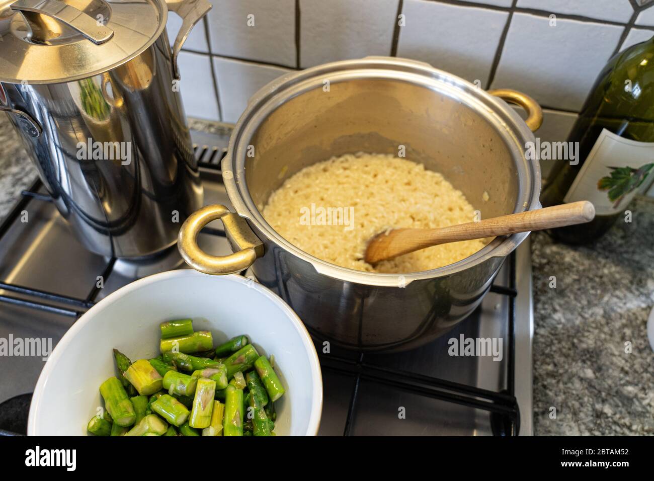 Risotto Reis mit Spargel, Zwiebeln und Weißwein kochen. Spargel in Scheiben geschnitten in einer Schüssel vor der Pfanne mit Reis. Hohe Winkelansicht. Stockfoto